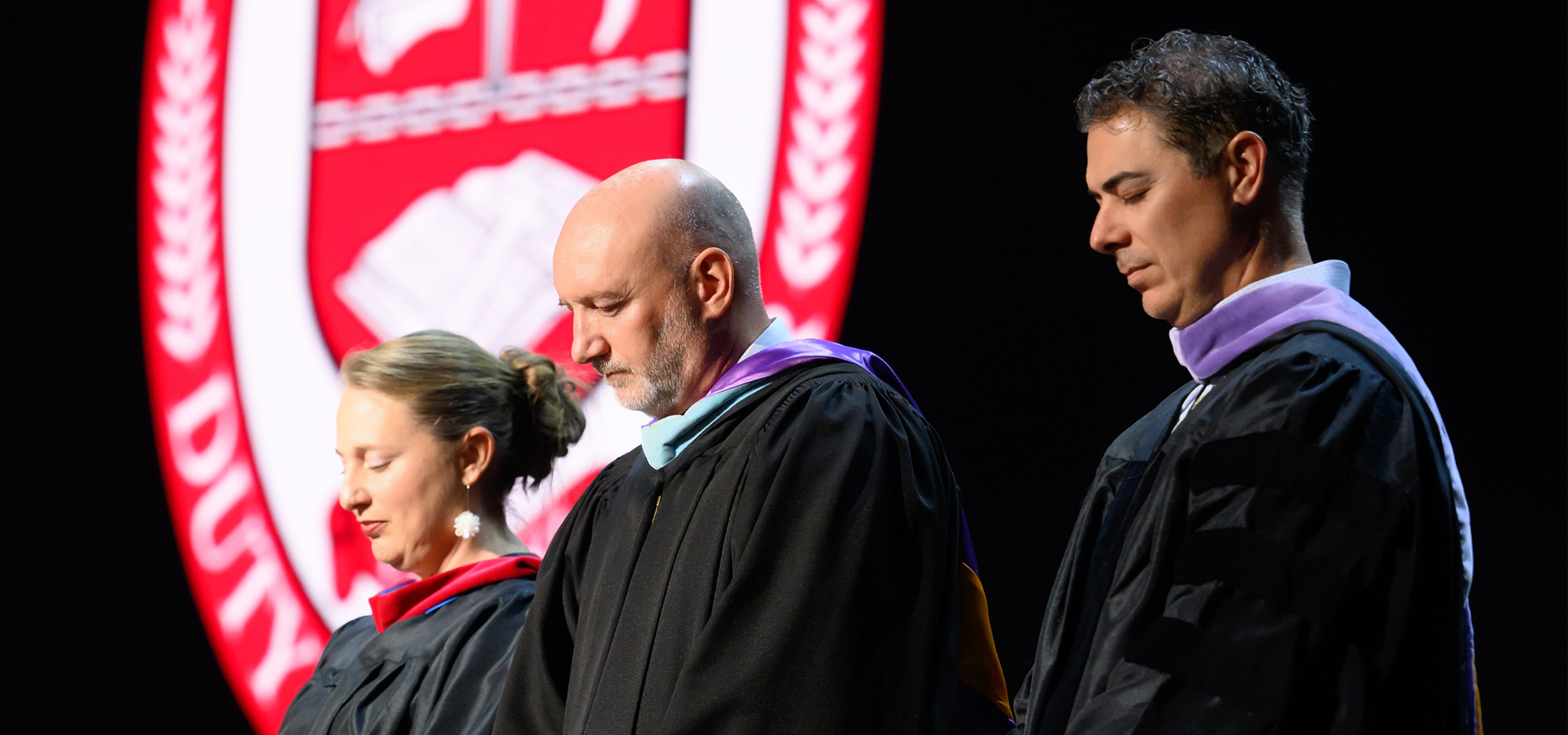 Three members of the Dunham leadership team praying at graduation.